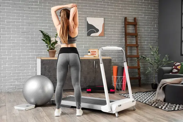Koşu bandının yanında antrenman yapan sportif bir kadın.