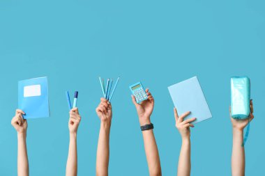 Mavi zemin üzerinde kırtasiye, hesap makinesi ve kalem kutusu olan birçok el