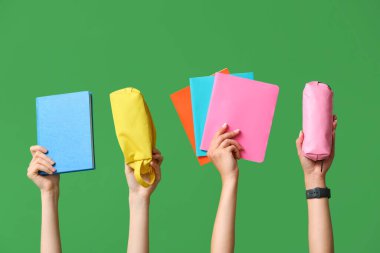 Yeşil zemin üzerinde not defterleri ve kalem kılıfları olan birçok el