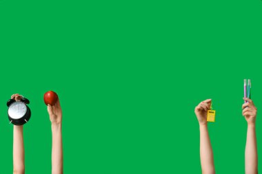 Yeşil zemin üzerinde kırtasiye, elma ve alarm saati olan birçok el