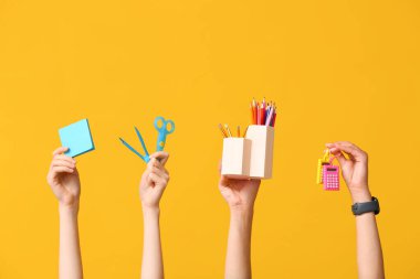 Sarı zemin üzerinde kırtasiye, yapışkan notlar ve hesap makinesi olan birçok el