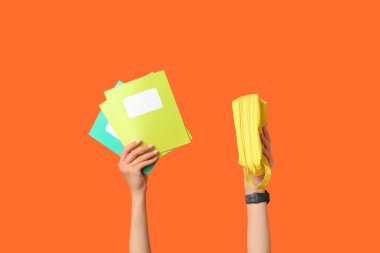 Turuncu arka planda defter ve kalem kutusu olan kadın elleri