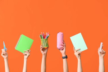 Kalem kutusu, kırtasiye malzemesi ve turuncu arka planda not defteri olan birçok el.