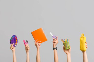 Kırtasiye malzemesi, defter ve kalem kutusu olan birçok el gri arkaplanda.