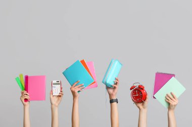 Gri arkaplan üzerine hesap makinesi, kırtasiye ve not defterleri olan birçok el