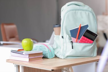 Sınıfta masada sırt çantalı ve kitaplı bir elma.