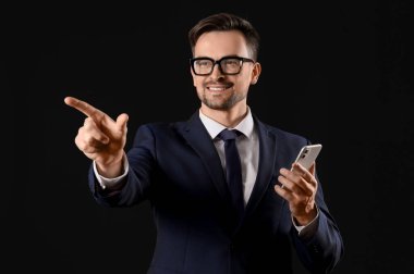 Cep telefonlu genç işadamı siyah arkaplanda sanal ekran kullanıyor