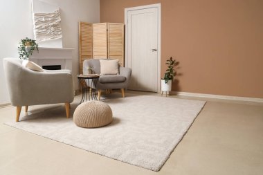 Oturma odasının içinde koltuklar, şömine ve yumuşak halı var.