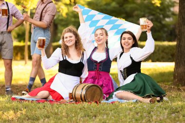 Ekim Festivali garsonları bira ve Bavyera bayrağıyla parkta çimlerde oturuyor.