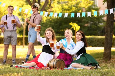 Ekim Festivali garsonları bira ve Bavyera bayrağıyla parkta çimlerde oturuyor.