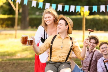 Geleneksel Alman kıyafetleri içinde genç bir çift ve bira ile Ekim Festivali 'ni dışarıda kutluyorlar.