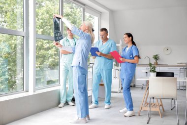 Klinikteki pencerenin yanındaki röntgen görüntülerini inceleyen bir grup doktor.