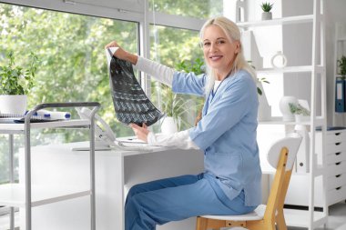 Klinikteki masada röntgen görüntüsü üzerinde çalışan kadın doktor.