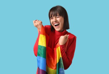 Mavi arka planda LGBT bayrağı olan mutlu genç bir kadın.