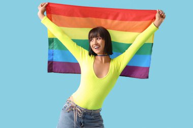 Mavi arka planda LGBT bayrağı olan gökkuşağı boğazlı mutlu genç bir kadın.