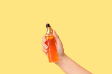 Sarı arka planda kozmetik ürünü şişesi olan bir kadın el.