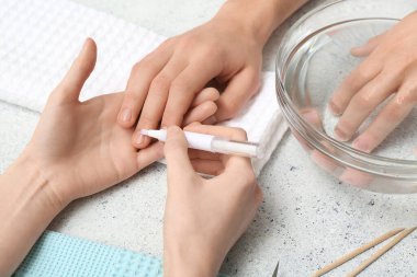 Manikür ustası, hafif grunge arka planında erkek tırnaklarına tırnak yağı sürüyor.