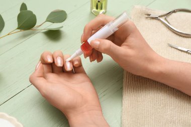 Tırnaklarına okaliptüs dalı ve yeşil ahşap arka planda havlu süren kadın elleri.