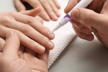 Erkek manikür ustası, gri arka plandaki kadın tırnaklarına manikür yağı sürüyor.