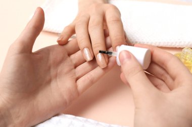 Manikür ustası, bej arka plandaki kadın tırnaklarına manikür yağı sürüyor.