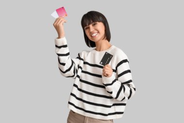 Gri arka planda kredi kartları olan mutlu genç bir kadın.