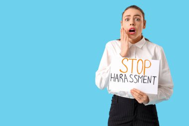 Elinde kağıt tutan genç iş kadını şok oldu mavi arka planda DUR HARASSMENT