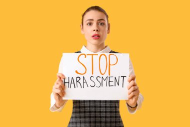 Sarı zemin üzerinde DUR HARASSMENT yazan kağıt tutan genç iş kadını