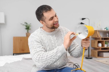 Genç adam evdeki masa lambasında ampul değiştiriyor.