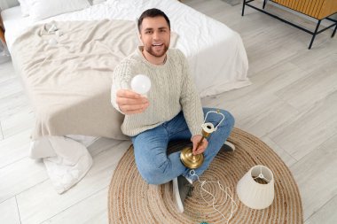 Genç adam evdeki masa lambasında ampul değiştiriyor.