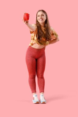 Pembe arka planda dolmalık biberli spor giyimli güzel bir kadın. Kilo verme konsepti