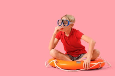 Yüzük şamandırası ve pembe arka planda ıslık çalan şnorkelli küçük çocuk cankurtaranı.