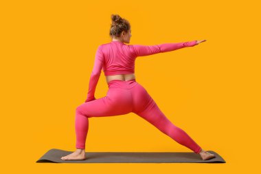 Sarı arka planda yoga yapan genç bir kadın.