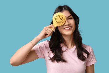 Mavi arka planda sarı saç fırçası olan güzel bir genç kadın.