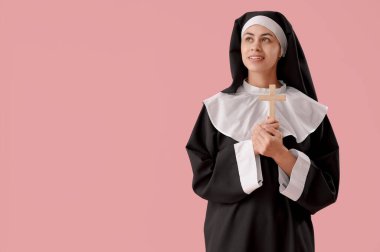 Pembe arka planda haç çizen genç rahibe