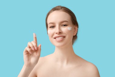 Kremalı genç kadın mavi arka planda bir şeye bakıyor.