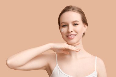 Kahverengi arka planda kremalı gülümseyen genç kadın.