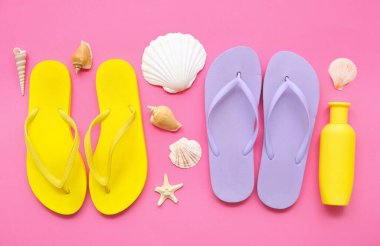 Pembe arka planda şık parmak arası terlikleri, güneş kremi ve deniz kabukları olan kompozisyon