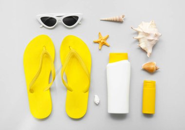 Plaj aksesuarları, güneş kremi ve gri arka planda deniz kabukları olan kompozisyon