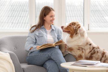 Evde sevimli bir Avustralya çoban köpeği olan genç bir kadın kitap okuyor.