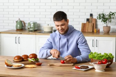 Genç adam mutfakta domates doğruyor.