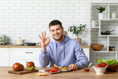 Genç adam lezzetli hamburgerler yapıyor ve mutfakta iyi görünüyor.