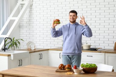 Lezzetli burgerli genç adam mutfakta iyi görünüyor.
