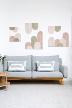 Oturma odasının içinde rahat bir kanepe, sehpa ve beyaz duvarda resimler var.