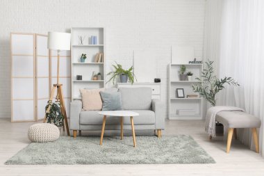 Katlanır ekran, gri kanepe, raf ünitesi ve sehpası olan şık bir oturma odası.