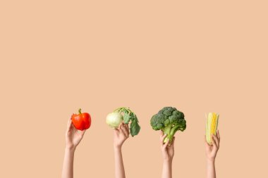 Female hands holding fresh vegetables on beige background
