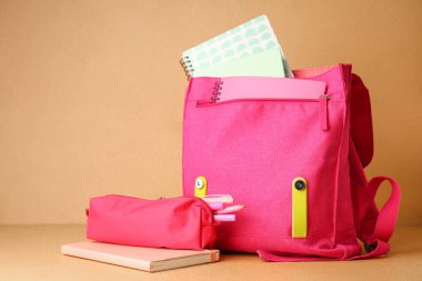 Masanın üzerinde bej rengi duvarlara karşı defter ve kalem kılıfı olan pembe bir sırt çantası.
