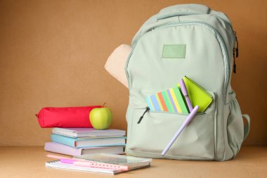 Sırt çantasında okul malzemeleri ve yeşil elma bej duvarda.