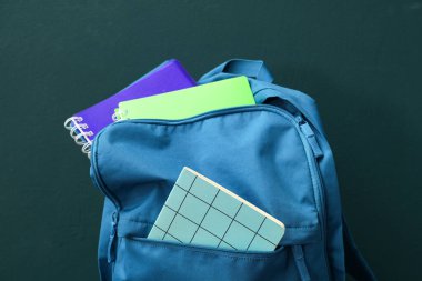 Koyu yeşil arka planda okul malzemeleriyle dolu sırt çantası.