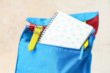 Masanın üzerinde beyaz grunge duvarına karşı not defteri olan mavi sırt çantası.