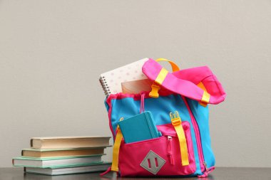 Gri arkaplana karşı defter ve kitaplarla dolu sırt çantası